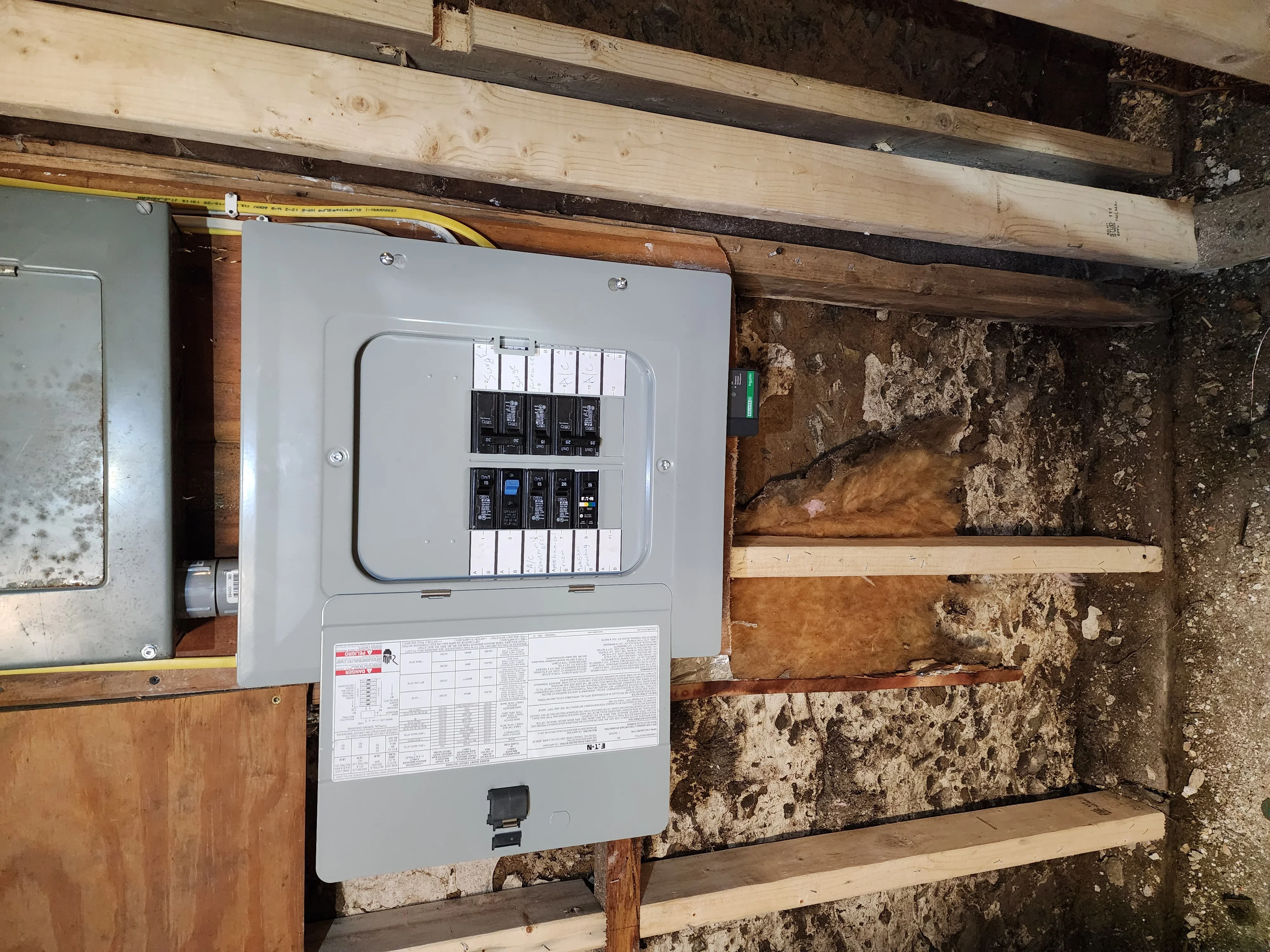 New electrical panel with circuit breakers installed on basement wall with wooden framing