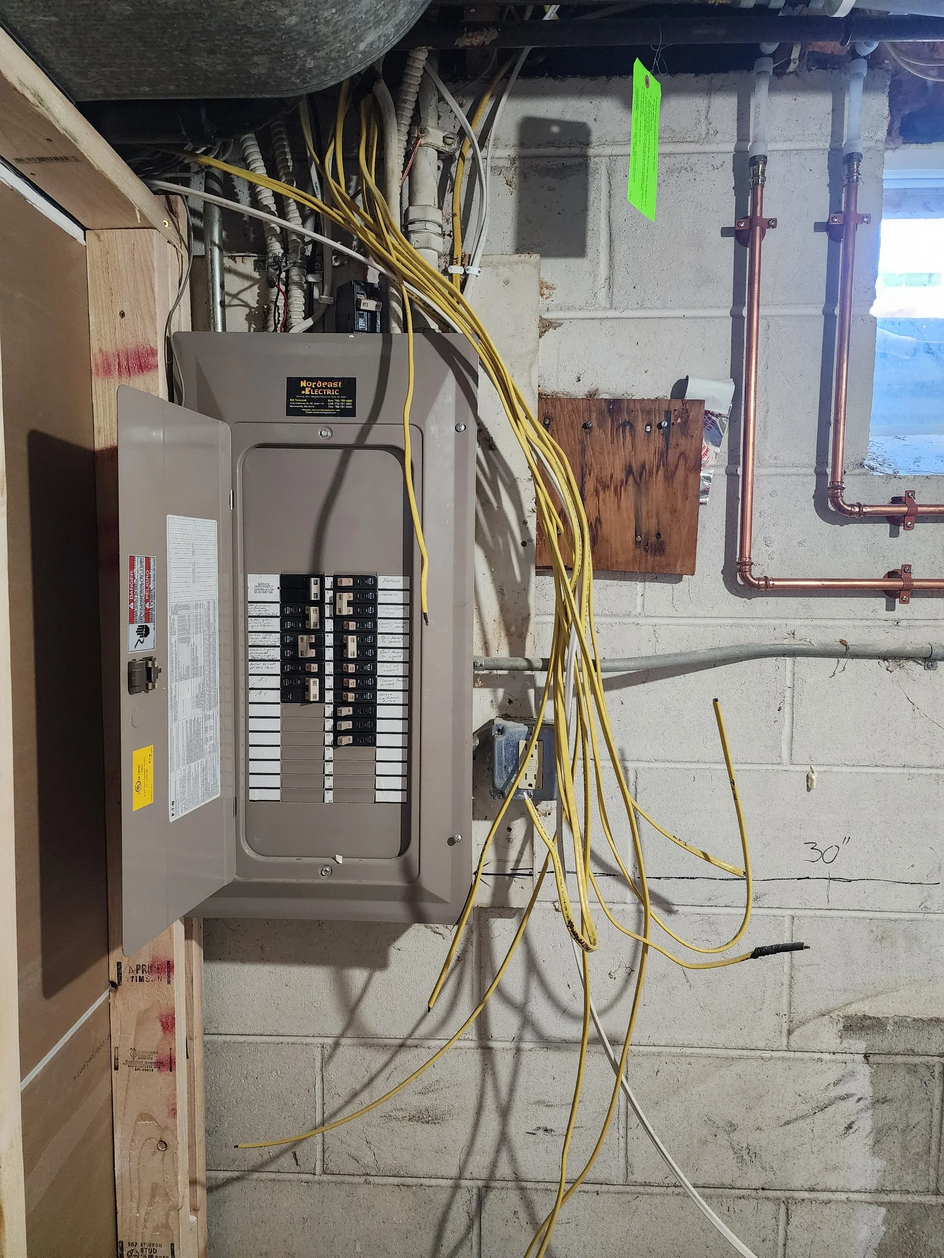 Electrical panel with breakers and yellow wire runs on concrete wall with copper piping
