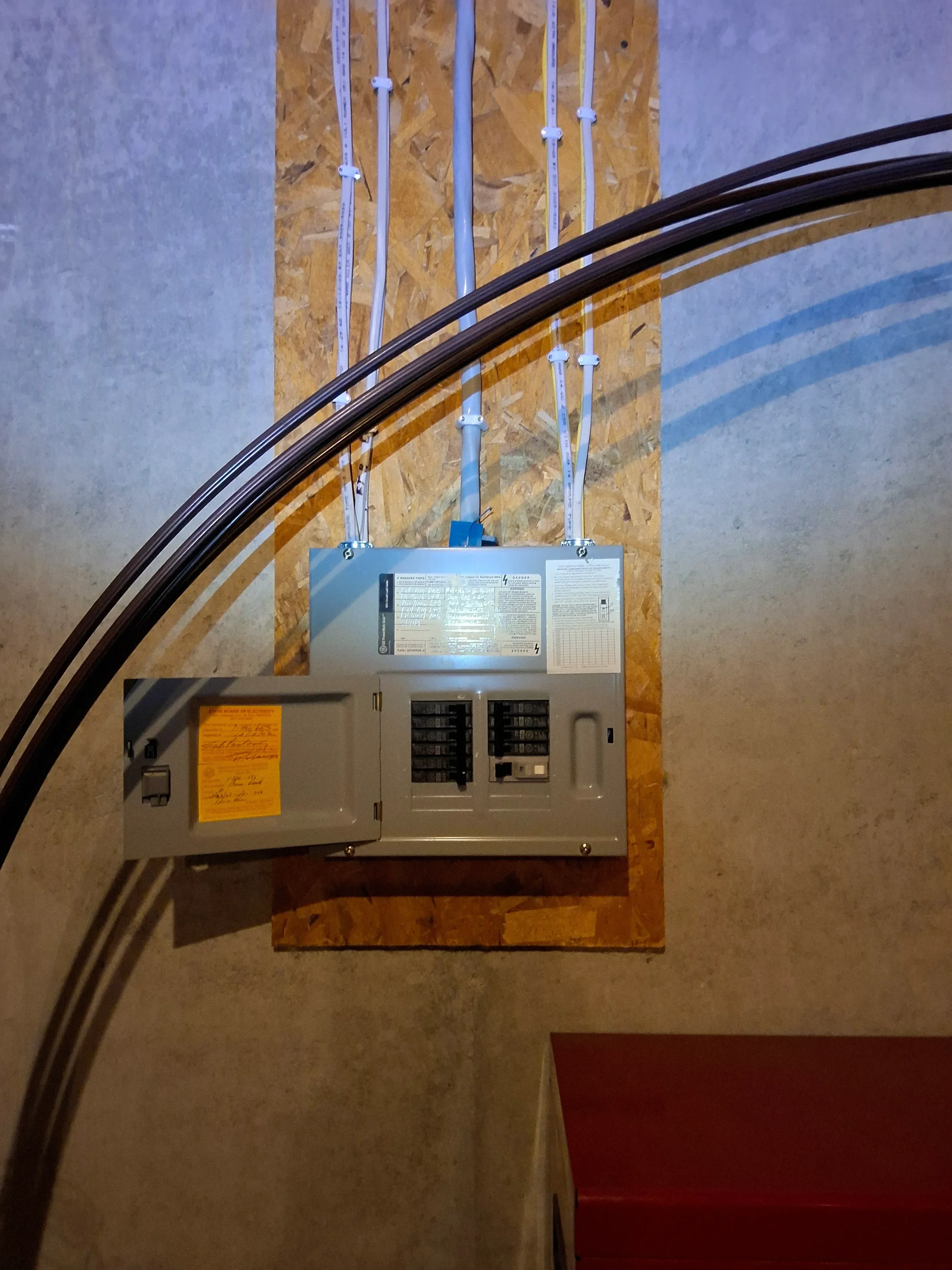 Electrical panel with circuit breakers and organized blue and black Romex wiring on OSB backing